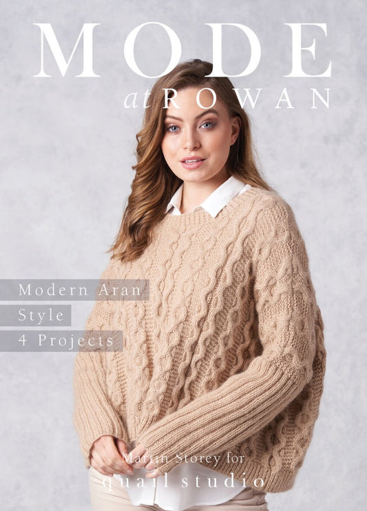 A woman wearing a cozy, beige cable-knit sweater with a white collared shirt underneath stands against a light gray background. Text reads "MODE at ROWAN," "Modern Aran Style," and "4 Projects." The tone is warm and inviting.