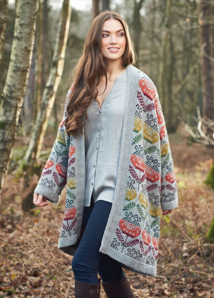 Woman strolling in autumn woods, wearing a colorful knit cardigan with floral patterns, blue jeans, and brown boots. She exudes a sense of serene contentment.