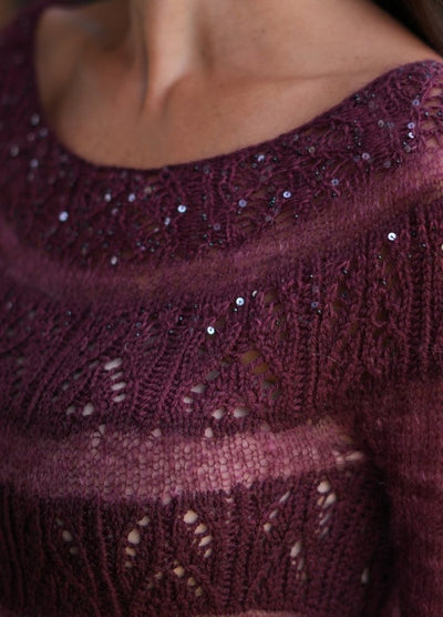 Close-up of a burgundy hand-knitted sweater adorned with shimmering sequins. The intricate lace pattern adds elegance and texture to the design.
