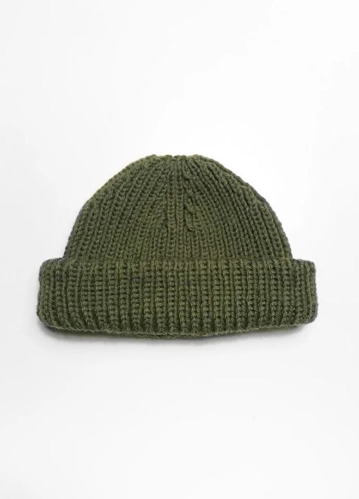 A green knitted beanie with a thick, folded brim is centered on a plain white background, conveying a simple, cozy, and minimalist feel.