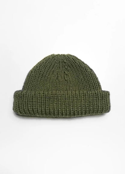 A green knitted beanie with a thick, folded brim is centered on a plain white background, conveying a simple, cozy, and minimalist feel.