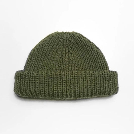 A green knitted beanie with a thick, folded brim is centered on a plain white background, conveying a simple, cozy, and minimalist feel.
