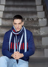 Man in a blue sweater and striped scarf, seated on stairs. The text reads "Rowan, New Nordic Men's Collection." The mood is stylish and contemplative.