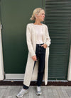 Woman in a cozy, cream cardigan over a white top and black jeans stands in front of a dark green door. Casual, relaxed pose, and calm atmosphere.