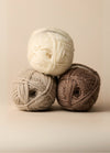 Three colourful balls of 100% wool yarn, ideal for crafting homewares or cozy slippers, displayed on a rustic surface.