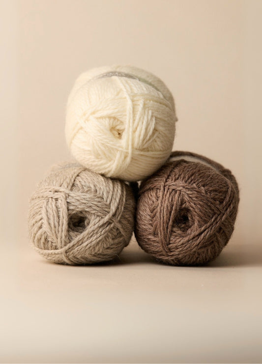 Three colourful balls of 100% wool yarn, ideal for crafting homewares or cozy slippers, displayed on a rustic surface.