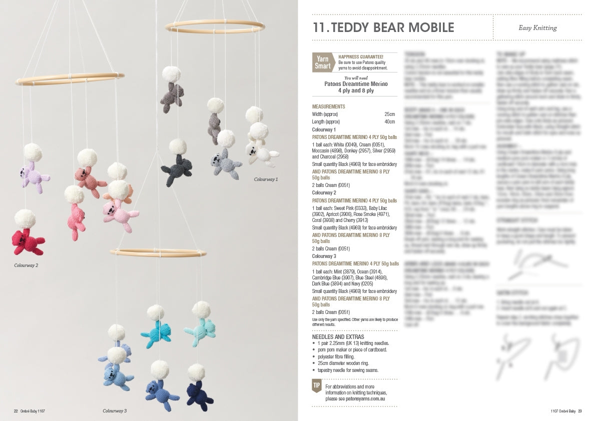 A mobile with small knitted teddy bears in pastel colours, hanging from wooden rings against a plain background. Instructions are blurred on the right. Keywords: knitting, mobile, teddy bears.
