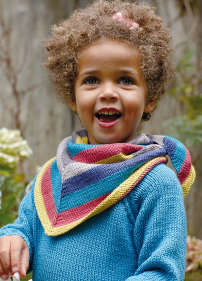 Child in striped Outlaw Neckerchief with blue sweater, outdoors with greenery.