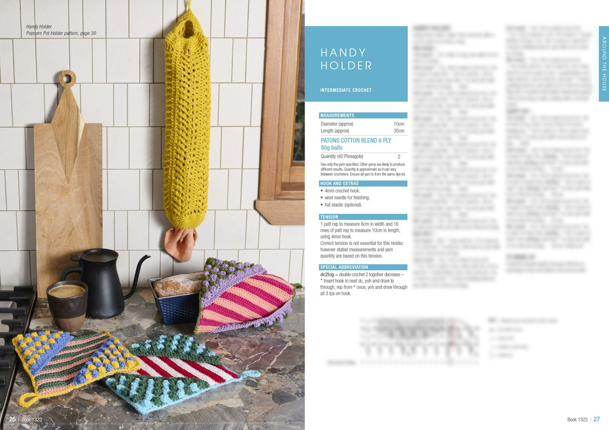 Hand-knitted pot holders in bright stripes and bobbles lie on a kitchen countertop with a teapot and cutting board. A yellow crochet holder hangs nearby. Cozy and colorful kitchen setting.