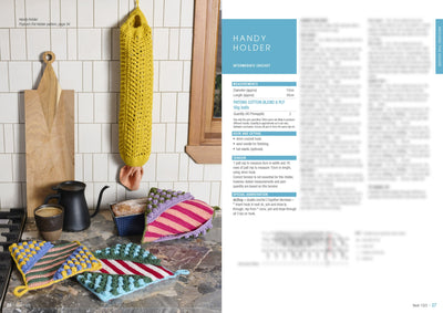 Hand-knitted pot holders in bright stripes and bobbles lie on a kitchen countertop with a teapot and cutting board. A yellow crochet holder hangs nearby. Cozy and colorful kitchen setting.