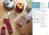 Wooden table with knitting supplies; a basket with yarn, another with oranges. Two knitted cases, red sock in progress, scissors, and needles. Cozy, crafty vibe.