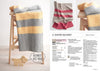 A knitted blanket with yellow and gray stripes is draped over a wooden ladder. Nearby, a wooden lion with a speech bubble reads "Beginner's Best Friend." A page on knitted blankets is on the right. Light, cozy atmosphere.