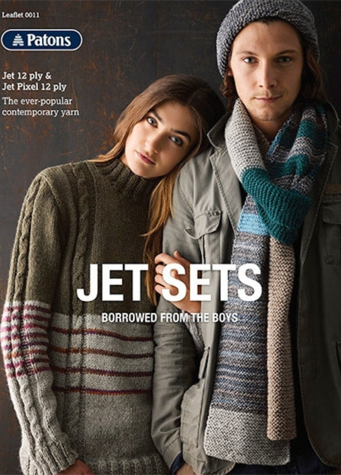 A woman and a man in cozy, knit sweaters and scarves pose stylishly. The text reads: "Patons Jet Sets, Borrowed from the Boys." Warm, casual vibe.