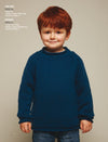 A child with red hair wearing a blue knitted sweater stands against a neutral background, smiling gently. The sweater style is detailed on the left.