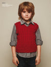 Young child with brown hair in a casual pose, wearing a red knit vest over a gray button-up shirt, expressing a calm and neutral demeanor.