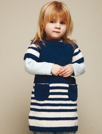 A young child with blonde hair stands against a neutral background, wearing a blue and white striped knit dress with pockets. The expression is calm and serene.