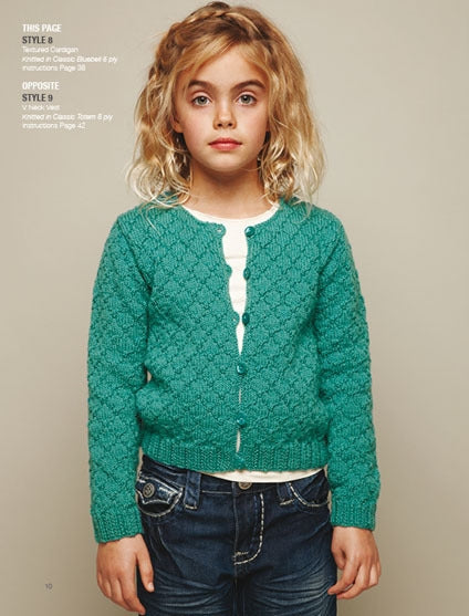 Young girl with curly blonde hair wearing a teal knitted cardigan over a white top and denim jeans, standing against a beige background, looks calm.