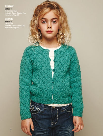 Young girl with curly blonde hair wearing a teal knitted cardigan over a white top and denim jeans, standing against a beige background, looks calm.
