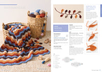 A cozy crochet blanket with wavy stripes in blue, orange, and brown is draped over a basket filled with colorful yarn balls, on a textured rug.