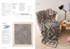 Cozy corner with a beige armchair draped in a blue and cream crocheted blanket. Matching pillow and open book on wooden table under a black lamp.
