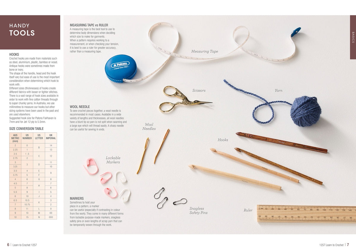 A collection of crochet tools on a table, including a tape measure, scissors, yarn, wool needles, hooks, markers, safety pins, and a ruler.