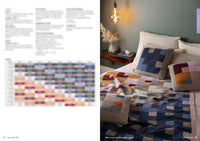 A cozy bedroom with a green wall features a knitted quilt and pillows with geometric patterns in blue, pink, and mustard. A warm overhead bulb adds a serene glow.