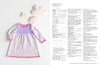 A pastel-colored knitted baby smock with pink trim lies on a textured white background with cloud decorations. Pattern instructions are visible on the right.