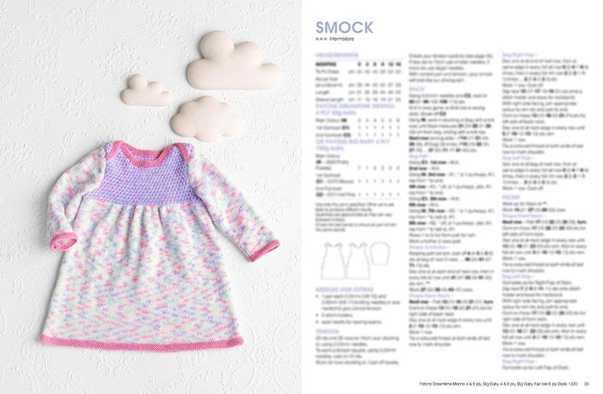 A pastel-colored knitted baby smock with pink trim lies on a textured white background with cloud decorations. Pattern instructions are visible on the right.