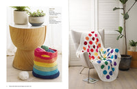 Cozy room with a knit rainbow basket on a wooden stool and yarn. Beside, a white chair holds a colorful polka dot blanket, conveying warmth.