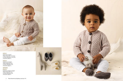 Two toddlers in cozy knit sweaters are sitting on a plush cream rug, exuding warmth and cuteness. One holds a soft toy; baby shoes and a giraffe toy are beside them.
