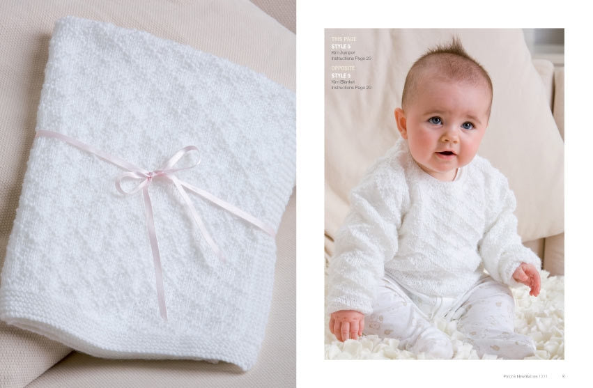 A baby in a white textured outfit is sitting on a soft surface, looking happy. On the left, a folded white blanket with a pink ribbon. Soft, cozy atmosphere.