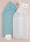 Two knitted baby sleeping bags, one blue and one white, with button closures. The blue is for 0-6 months and the white for 9-12 months. A small toy is above them.
