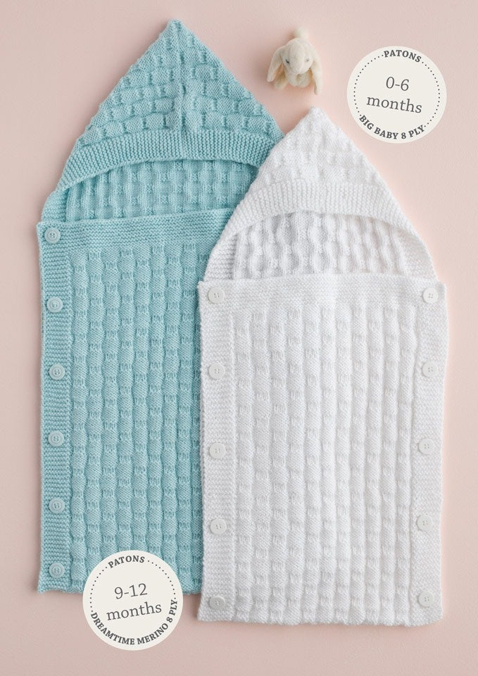 Two knitted baby sleeping bags, one blue and one white, with button closures. The blue is for 0-6 months and the white for 9-12 months. A small toy is above them.