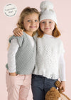 Two young children smile while posing together against a soft pink background. One wears a knitted gray vest, the other in a white sweater and pom-pom hat.