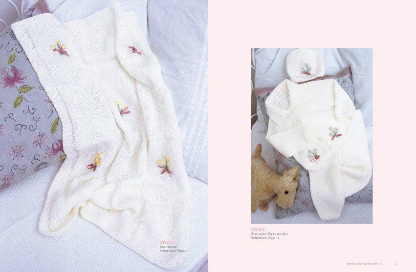 A soft white knitted baby blanket with floral embroidery rests on a floral pillow, paired with a matching cardigan and hat on a bed, exuding warmth and coziness.