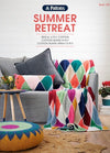 Cozy living room with a colorful patchwork blanket draped over a gray armchair. A matching cushion, plants, and yarn pouf add to the cheerful vibe.