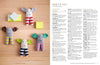 Colorful knitted elephants with striped legs and cheerful smiles lie on a wooden surface with small yellow and white blocks. Text on the right reads "BABY'S TOY" with crochet instructions. The scene is playful and inviting.