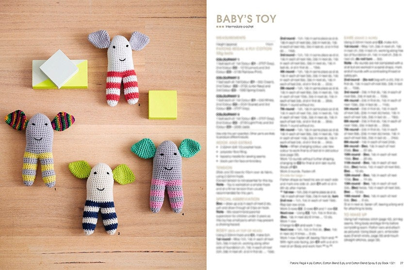 Colorful knitted elephants with striped legs and cheerful smiles lie on a wooden surface with small yellow and white blocks. Text on the right reads "BABY'S TOY" with crochet instructions. The scene is playful and inviting.