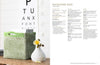 A crochet magazine bag in light green sits on a wooden table beside a white vase with yellow flowers. An eye chart is in the background.