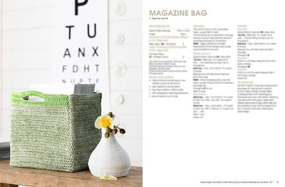 A crochet magazine bag in light green sits on a wooden table beside a white vase with yellow flowers. An eye chart is in the background.