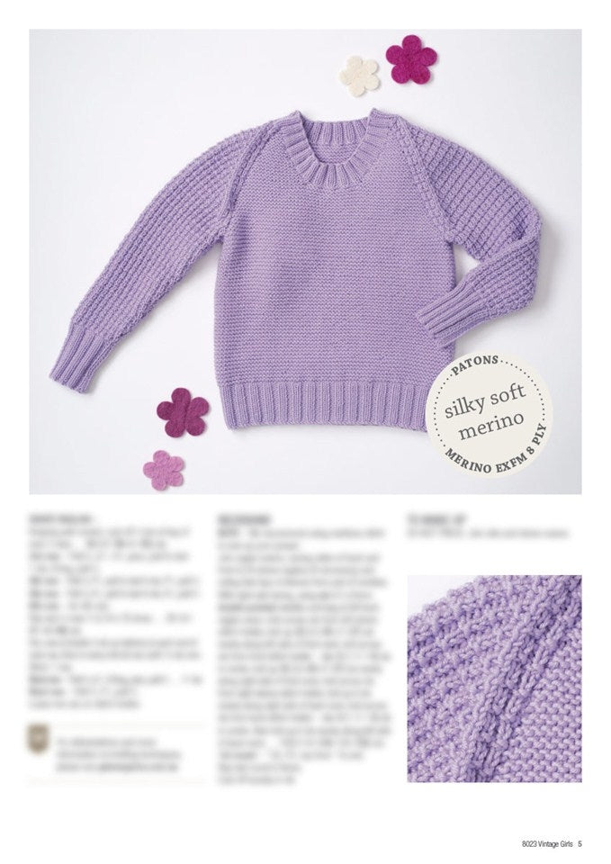 Lavender knitted sweater with textured sleeves, surrounded by purple and white felt flowers. Label reads "silky soft merino." Close-up detail shown.