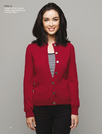 Smiling woman wearing a red buttoned cardigan over a black-and-white striped top stands against a gray background, conveying a casual, cheerful tone.