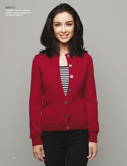 Smiling woman wearing a red buttoned cardigan over a black-and-white striped top stands against a gray background, conveying a casual, cheerful tone.