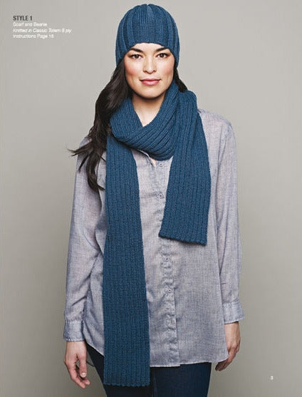 A woman in a blue knit hat and matching scarf over a light gray button-up shirt stands against a plain background, conveying a cozy, casual vibe.