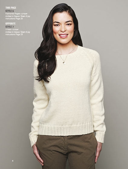 Smiling woman wearing an ivory knit sweater and olive pants, standing against a gray background. Her long, dark hair is styled in waves.