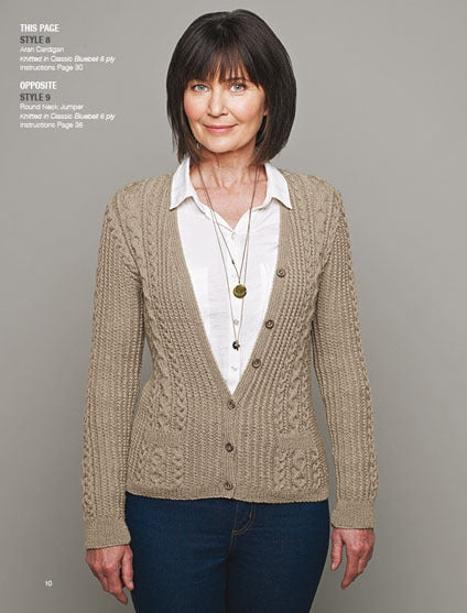 Woman wearing a beige knit cardigan over a white shirt, with long necklaces, standing against a gray background. She has a calm and confident expression.