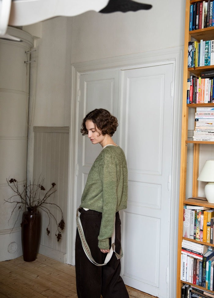 Cidreira Sweater: green knit sweater worn with dark pants, photographed from behind in a room with bookshelves and dried branches.