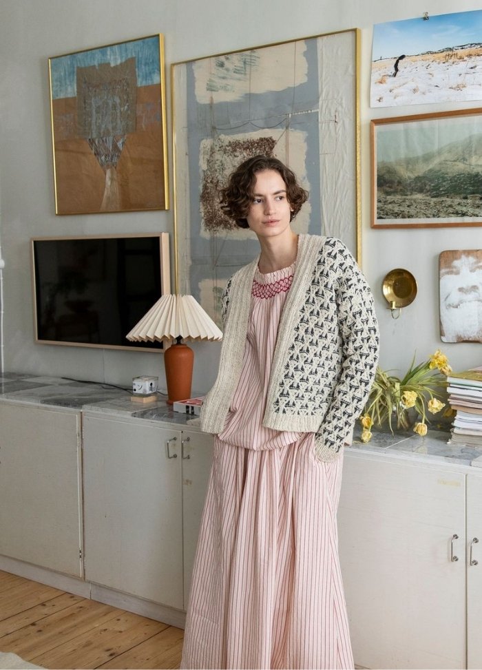 Cobogo Cardigan: white cardigan with black geometric patterns, layered over a striped dress, photographed in a room with framed art and vintage decor.