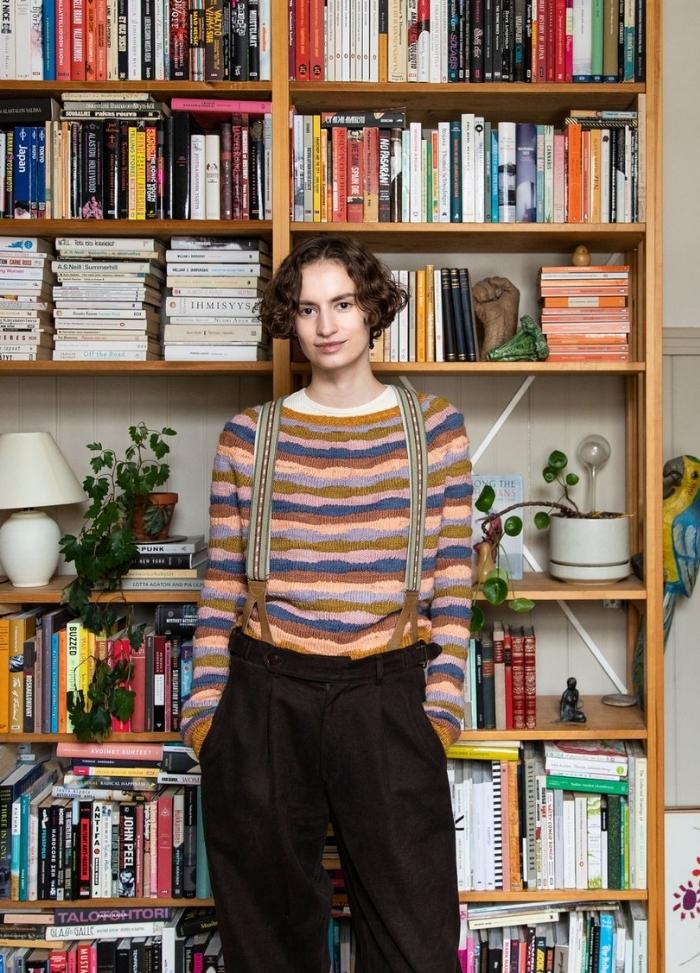 Espedito Sweater: colorful striped knit sweater worn with suspenders and dark pants, photographed in front of a bookshelf.