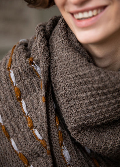 Lygia Shawl: brown knit shawl with white and orange decorative patterns, photographed in a close-up view.